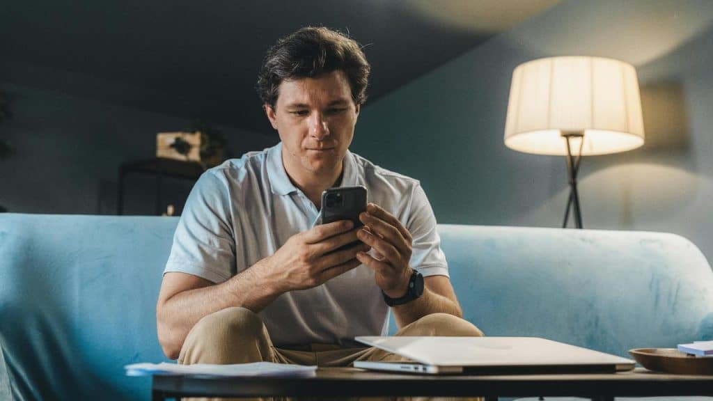 A man sitting on a couch, looking thoughtfully at his phone.