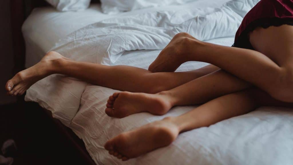 A couple lying on a bed with their legs gently intertwined.