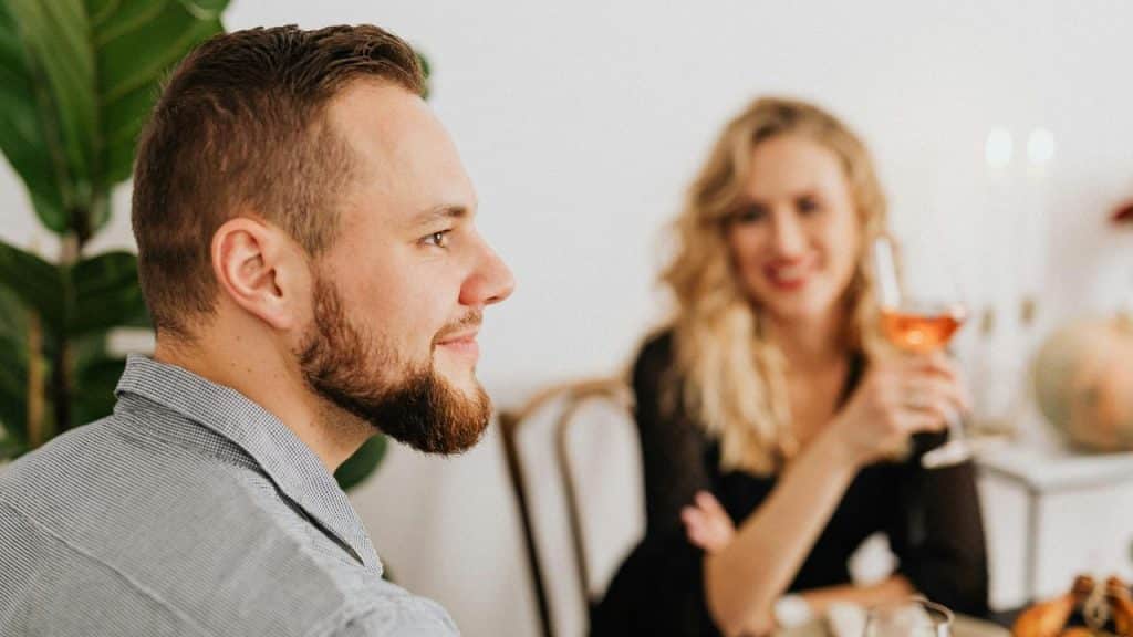 A woman gazes at a man while holding a wine glass.