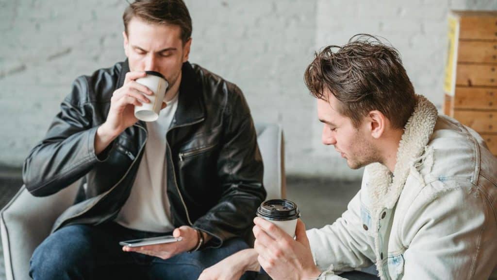 A photo of two men drinking coffee together while looking at a phone.