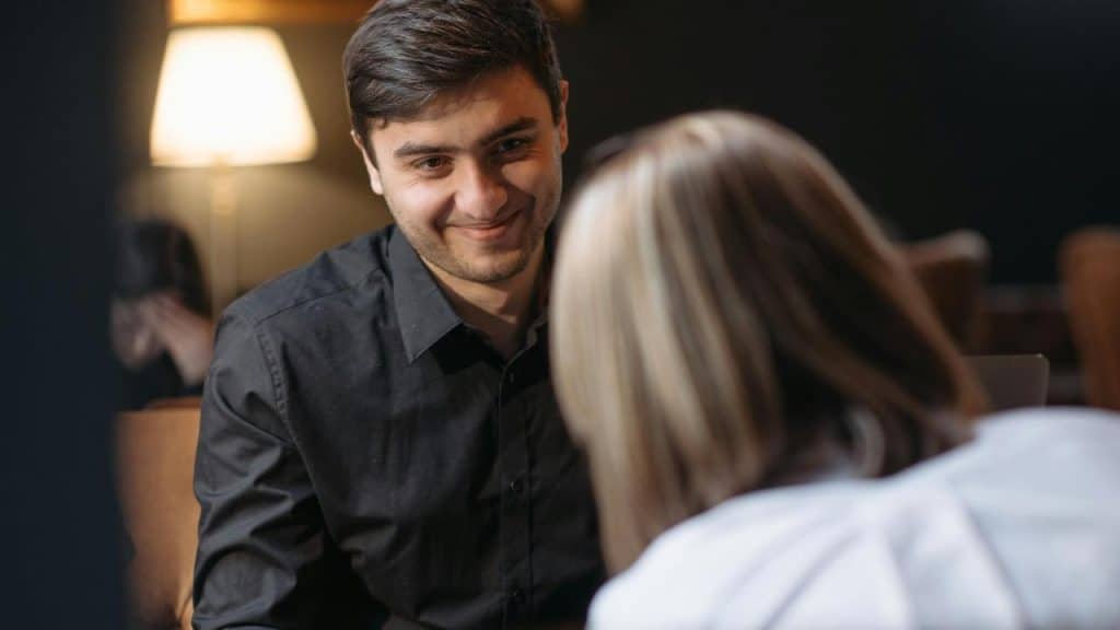 A man smiling across the table from a woman in a softly lit setting.