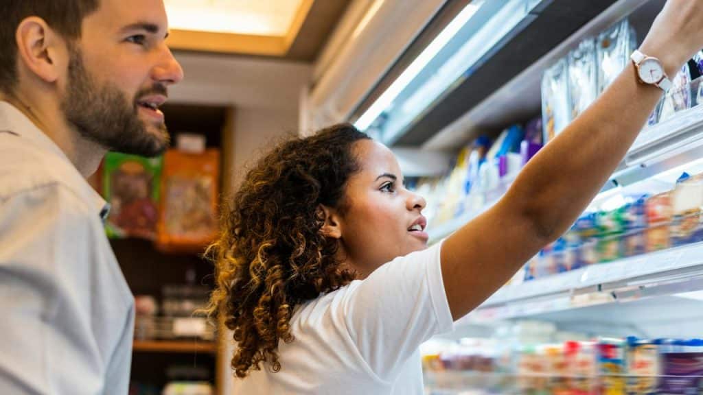 A woman reaches for an item on a store shelf as a man stands nearby.