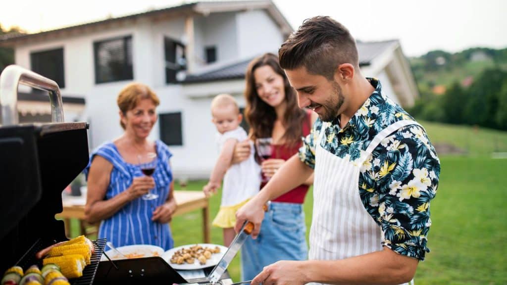 A man tends the grill outdoors while two women are on the background.