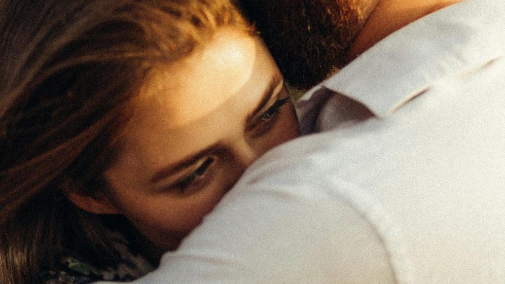 A woman leans her head on a manโs shoulder as they share a quiet embrace.