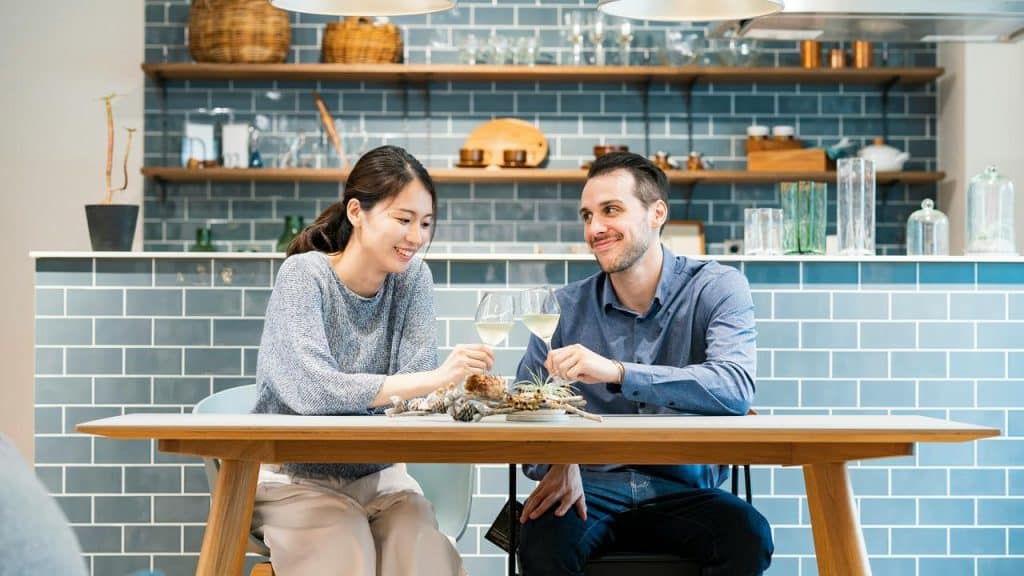 A couple sits together at a kitchen table, sipping drinks and talking.