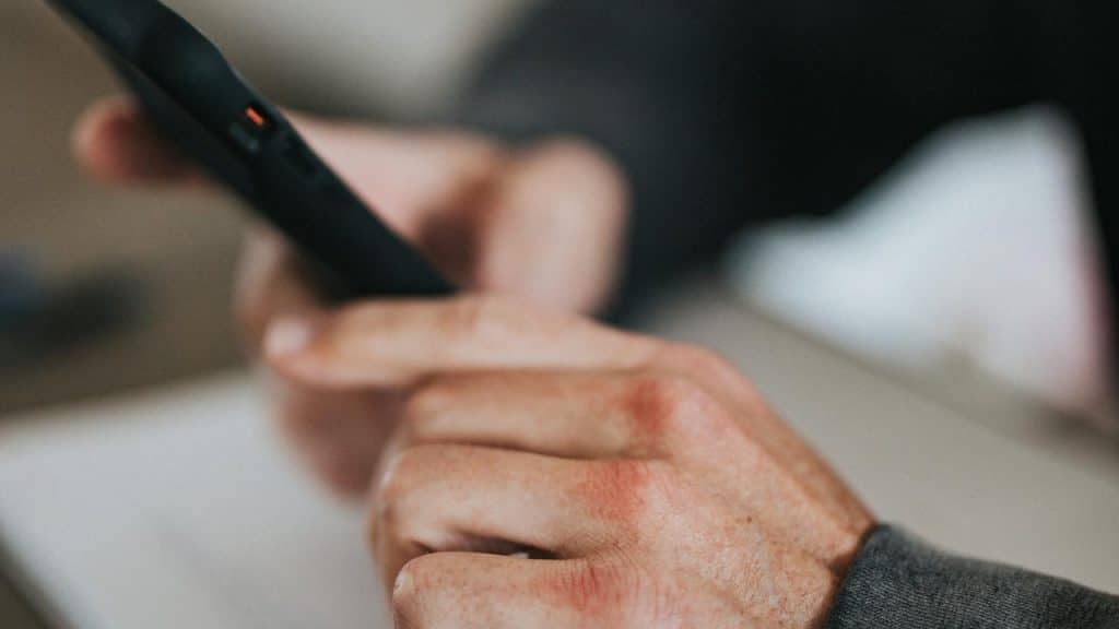 A person scrolls on a smartphone, holding it securely with both hands.