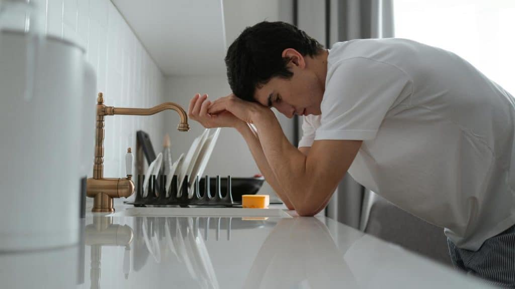 A man leans against a kitchen counter, looking tense and stressed.