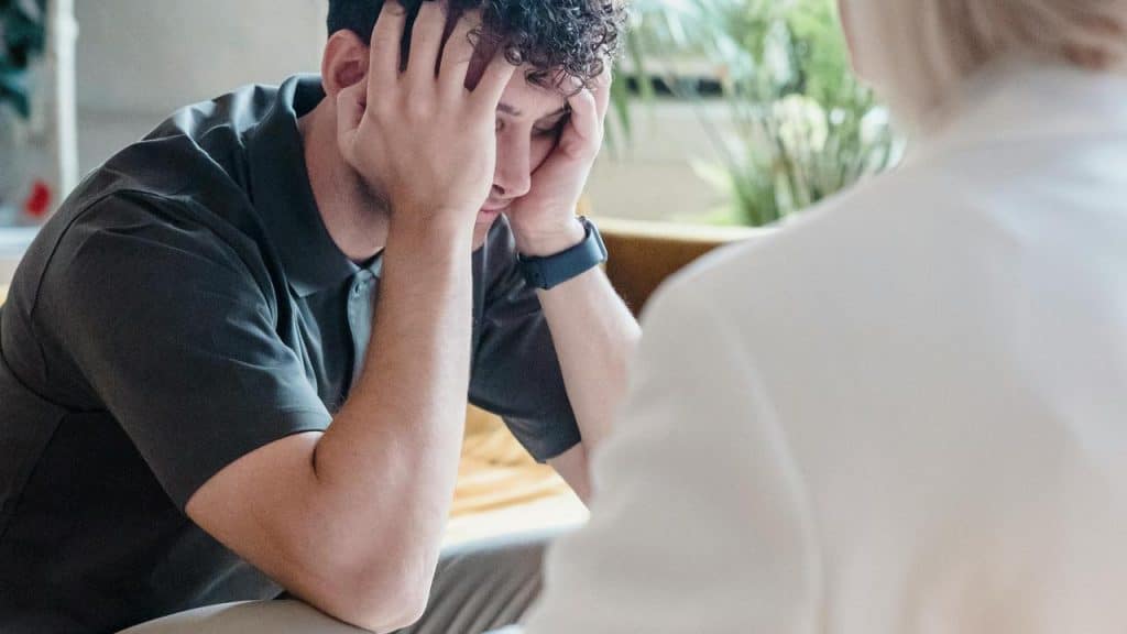 A man sits hunched over, covering his face with his hands in frustration.