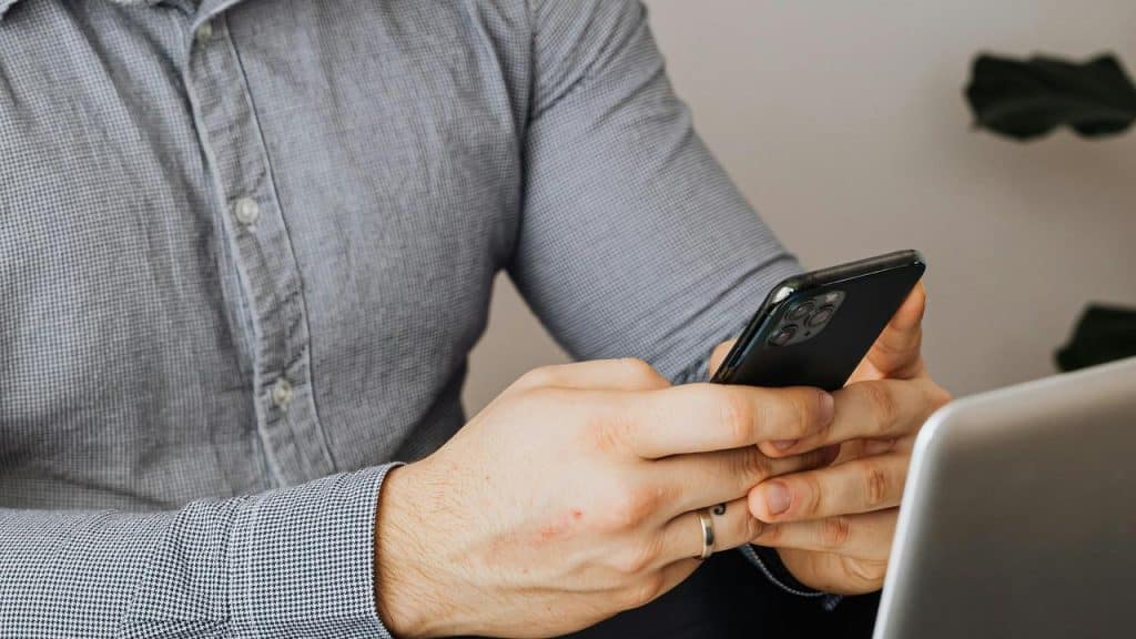 A man sits at a desk, scrolling on his phone.