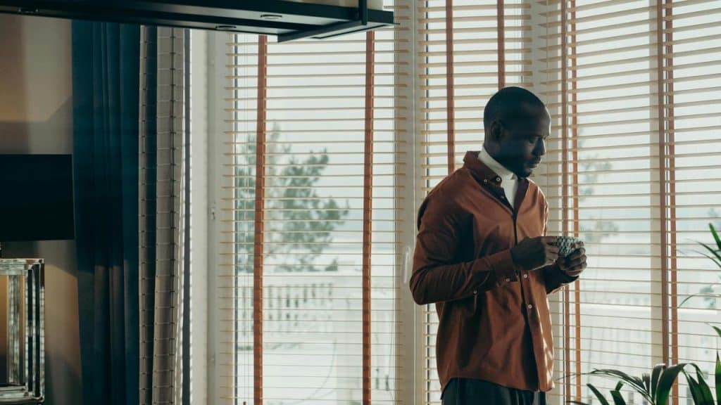 A man stands by the window, quietly holding a cup and thinking.