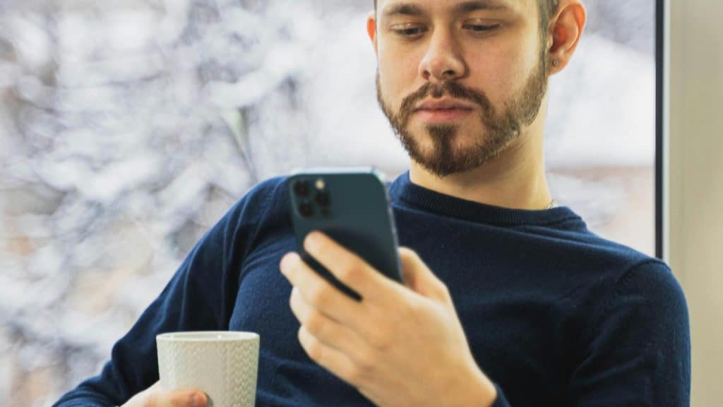 A man holds a coffee cup and glances at his phone.