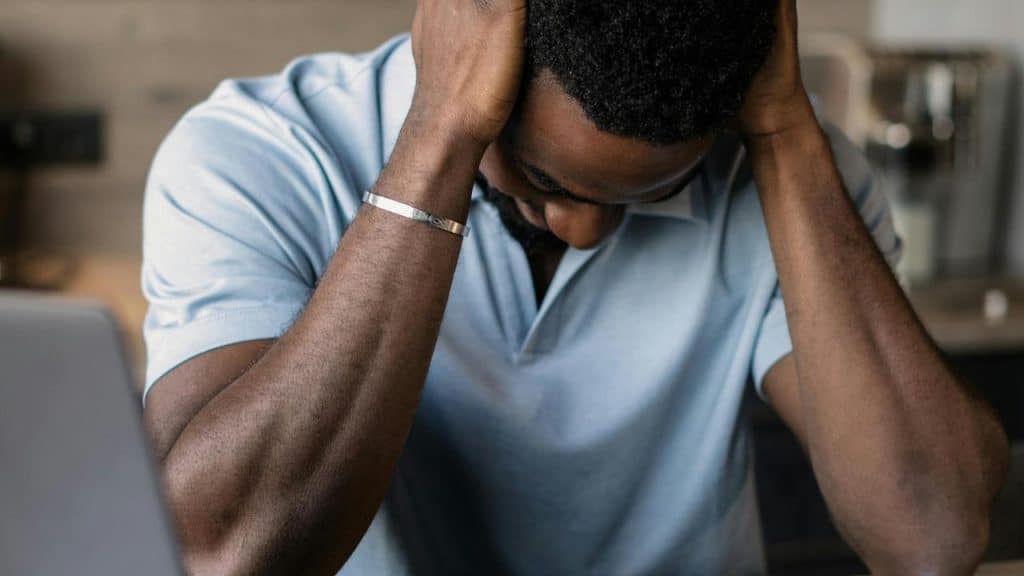 A man leans forward with his hands on his head.