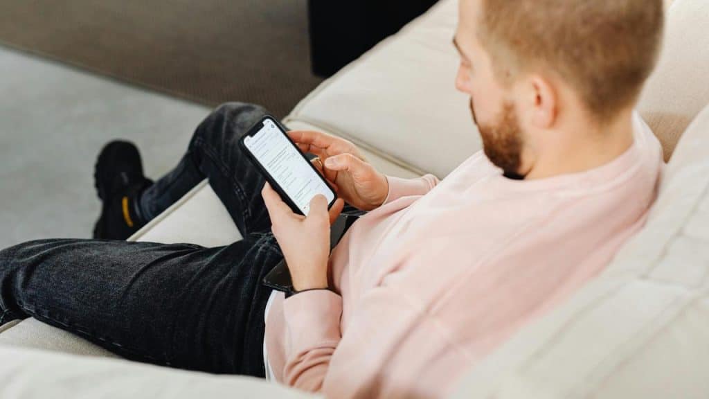 A man lounges on a couch, phone in hand, checking his messages.