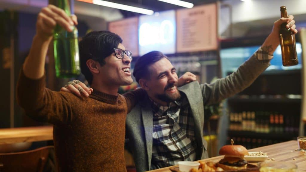 A photo of two friends laughing and toasting with beers at a lively bar.