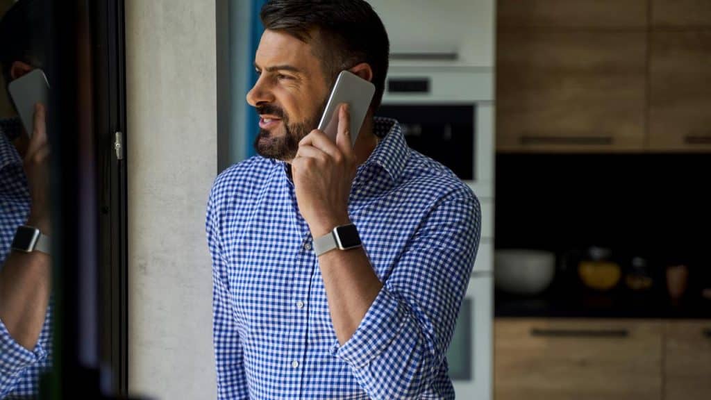 A man stands near a window, talking on his phone.