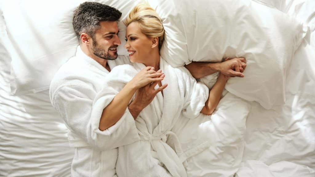 A couple looking at each other and smiling while laying in bed.