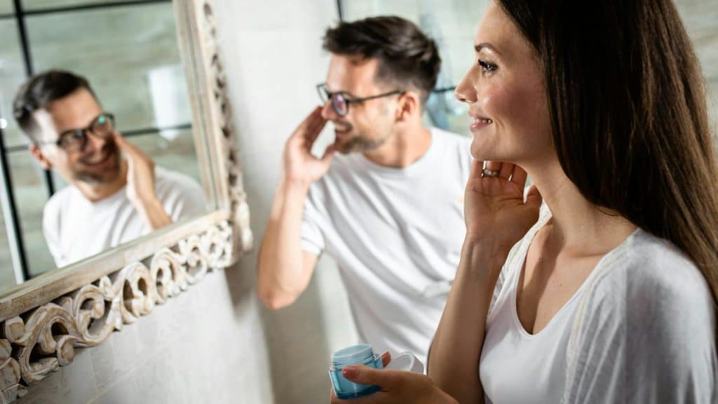 A couple smiling at their reflection while doing skincare together.Comparing her to anyone else, your ex, a coworker, or a stranger online, will scar the relationship and plant seeds of doubt into her mind.