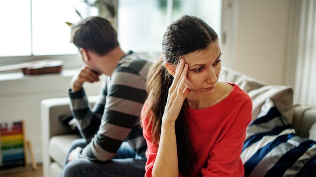 A couple having an argument, with the woman looking distressed in the foreground and the man turning his back on the couch.