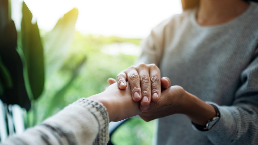 A close-up of one person's hands gently holding and comforting another person's hand.
