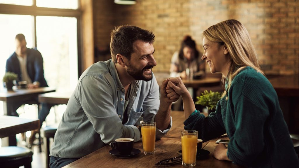 A happy couple communicating and holding hands while being on a date in a cafe.