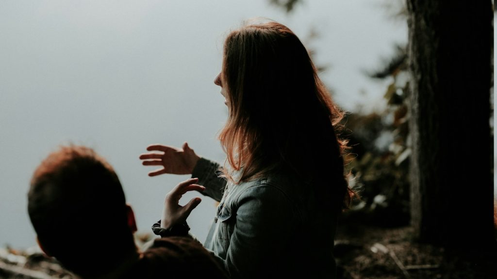 The woman wearing a gray jacket is talking to a man.
