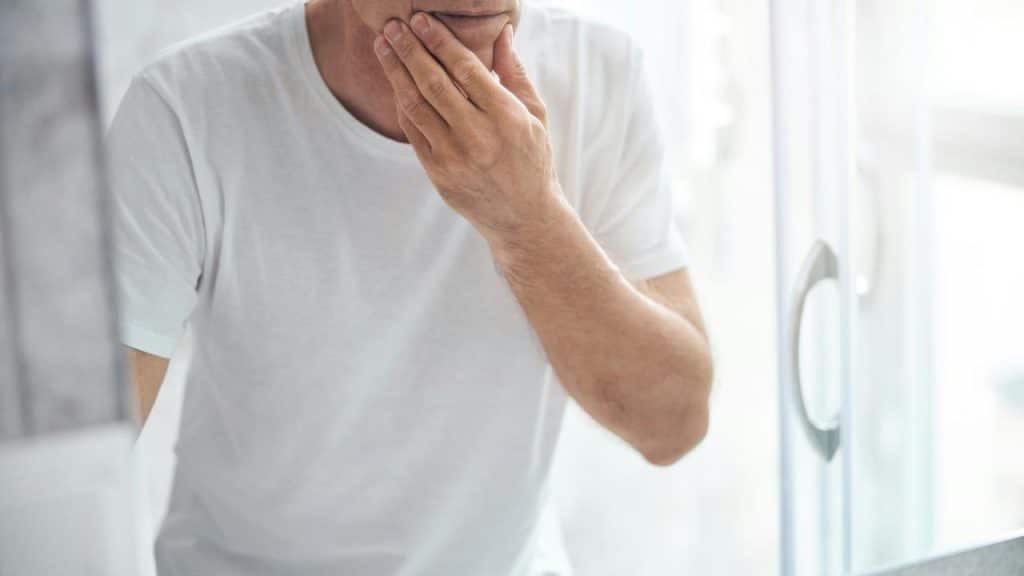 A man looks at himself in a bathroom mirror.