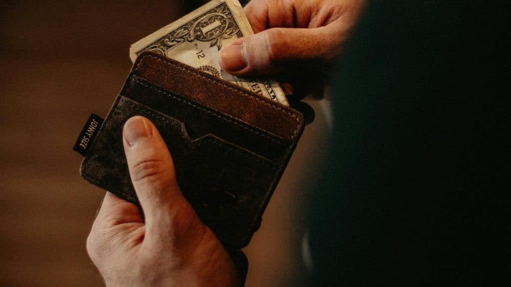 A person puts a dollar bill into a leather wallet.