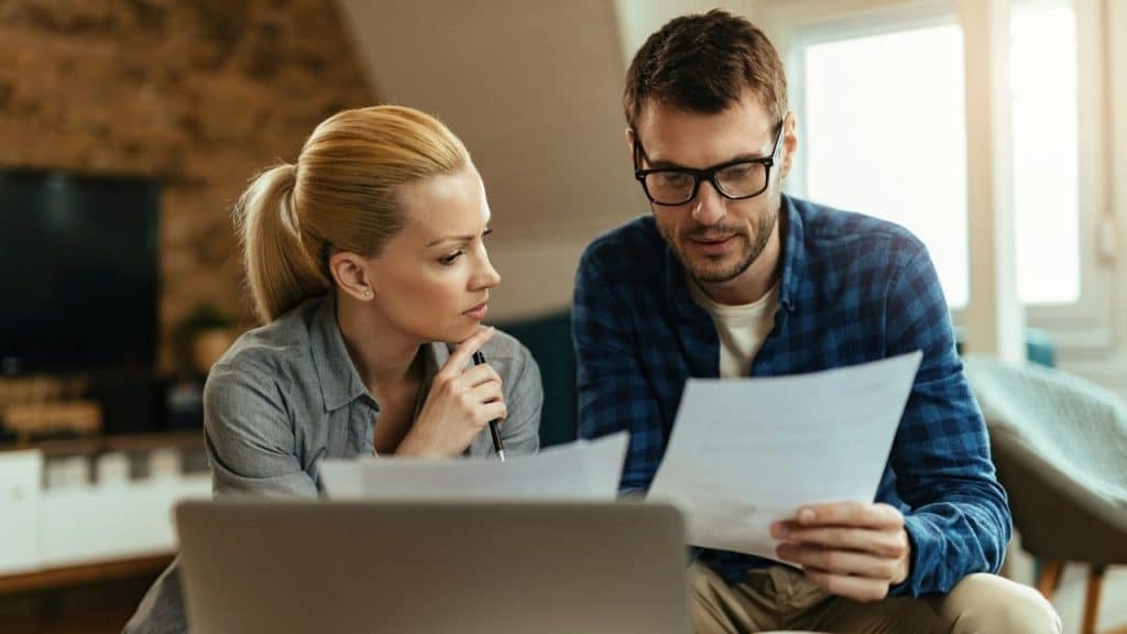 Serious couple reviewing documents together, sitting in front of an open laptop.