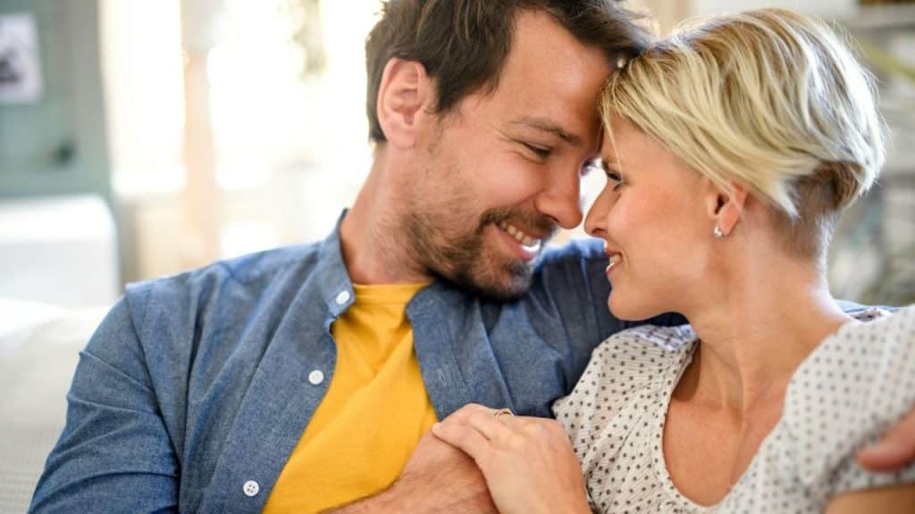 A smiling man and woman are holding hands and touching foreheads affectionately.
