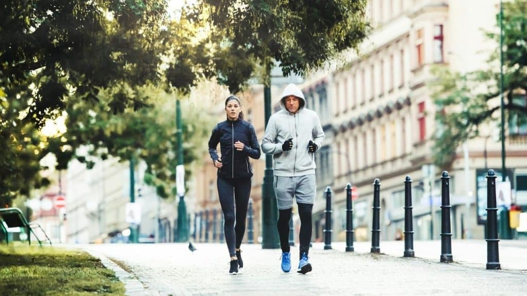 A man and a woman in athletic wear are running side-by-side on a city street.