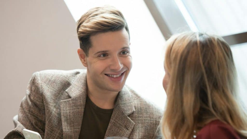 Smiling man with highlighted hair in a plaid jacket talking closely to a woman.