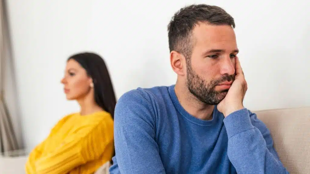 A sad man in blue and a woman in yellow sitting back-to-back, looking away.