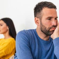 A sad man in blue and a woman in yellow sitting back-to-back, looking away.