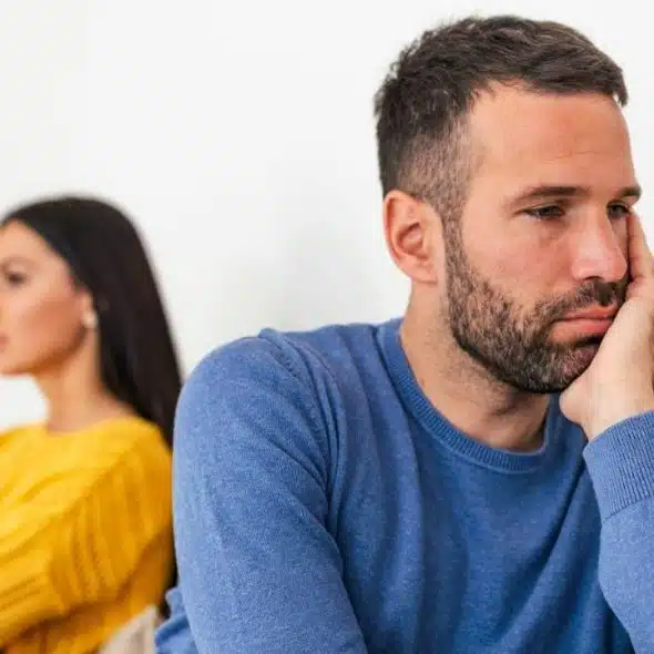 A sad man in blue and a woman in yellow sitting back-to-back, looking away.