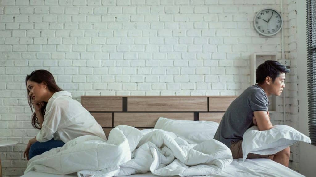 Man and woman sitting on a bed with their backs to each other after a disagreement.