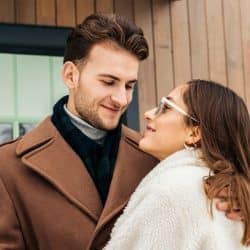 Couple warmly embracing and smiling at each other in front of a modern wooden house.