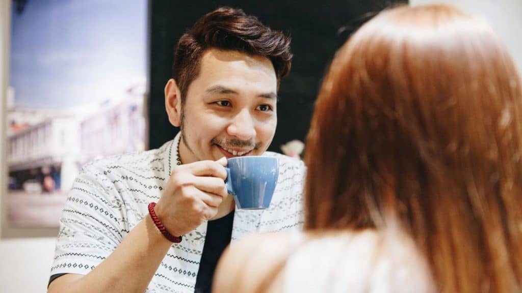 Smiling man holding a blue mug while talking to a woman with long red hair.