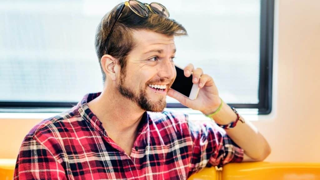 Smiling man in a red plaid shirt talking on a mobile phone indoors.