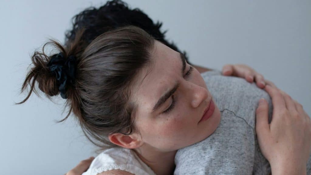 Close-up of a woman with her eyes closed embracing a person in a grey shirt.