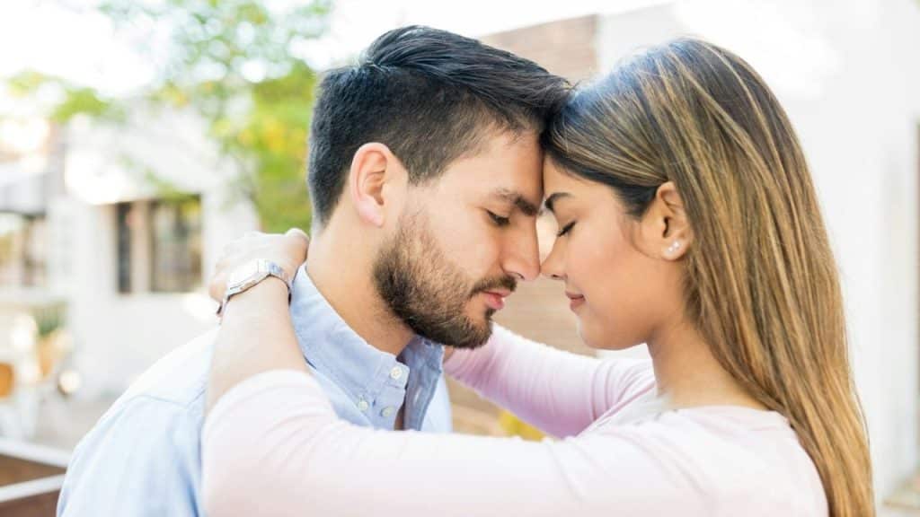 Couple with eyes closed embracing and touching foreheads outdoors.