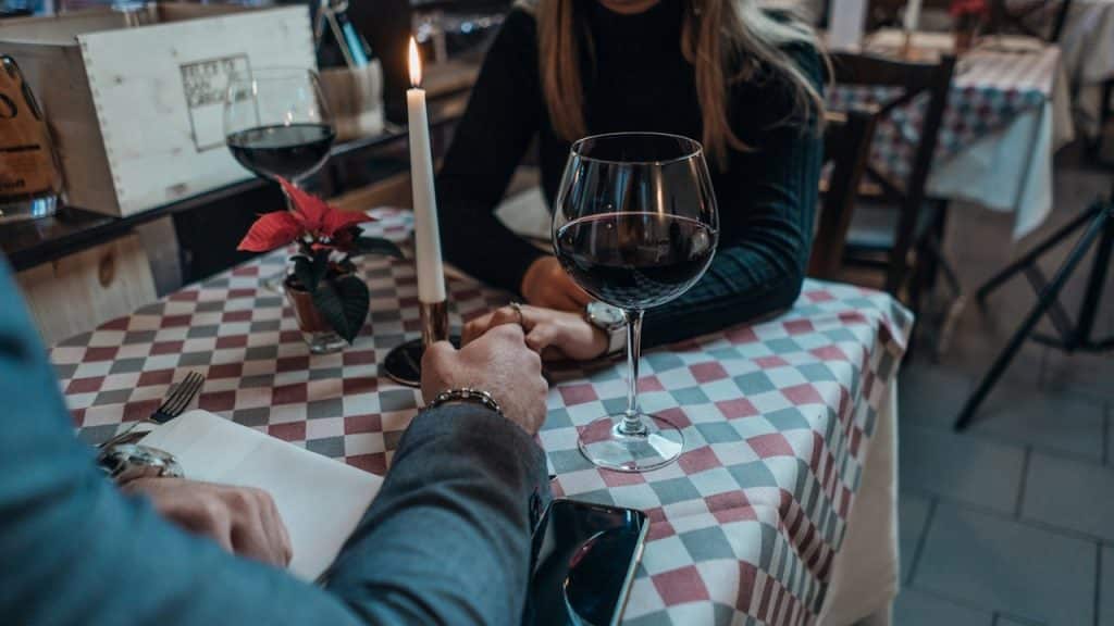 A man and a woman are sitting at a table in a restaurant, holding hands over a checkered tablecloth.