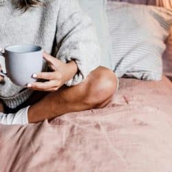 A person sitting on a bed holding a mug with both hands.