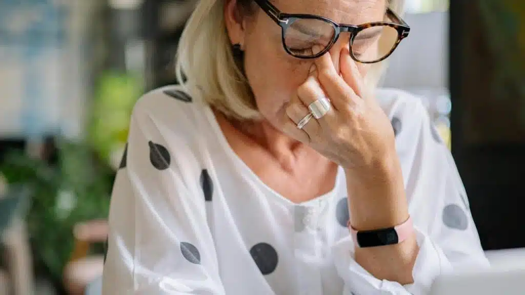 A woman wearing glasses pinching the bridge of her nose in frustration or fatigue.