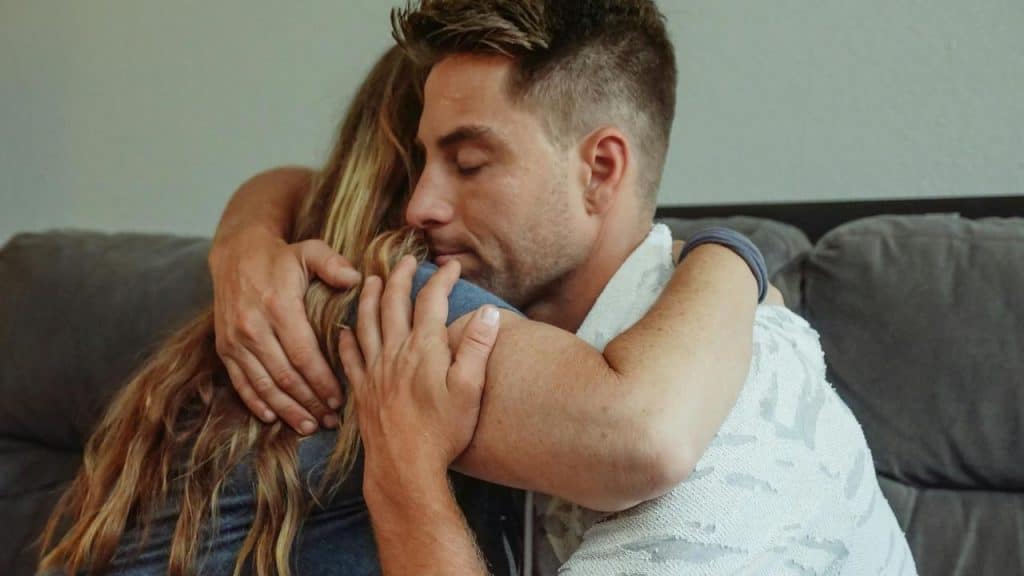 A man and woman embracing each other in a comforting hug on a couch.