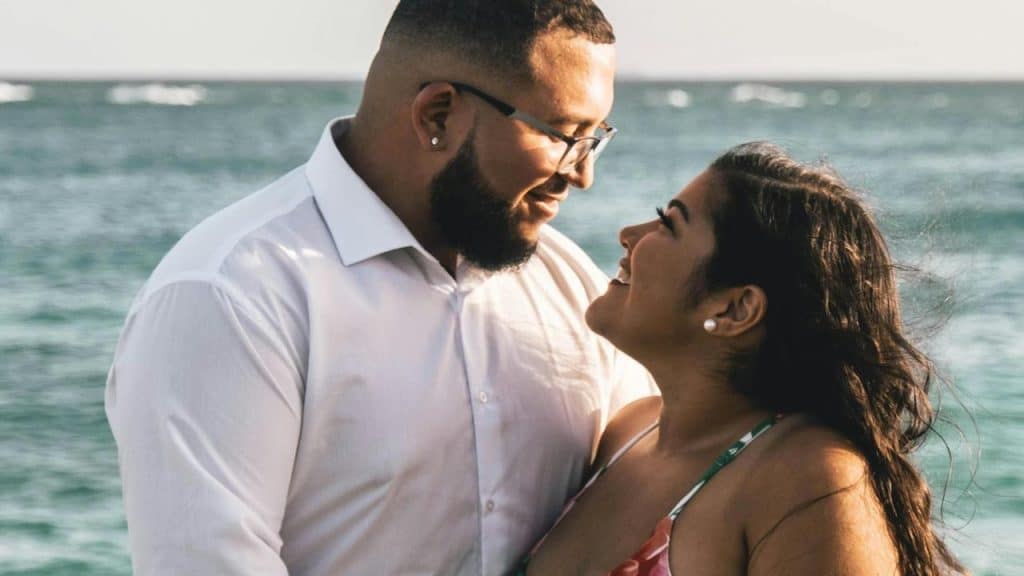 A couple standing by the ocean smiling lovingly at each other.
