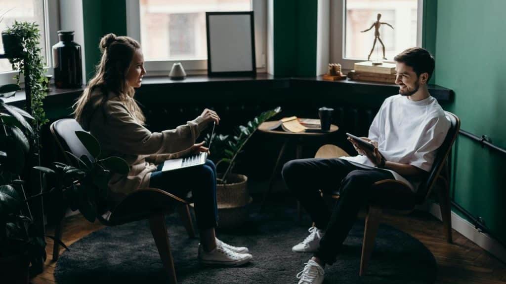 A man and woman sitting in chairs facing each other and talking in a cozy room.