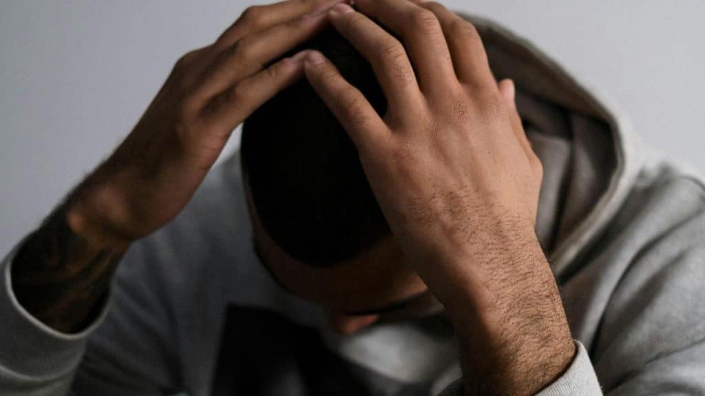 A man sitting with his head down and hands on his head in distress.