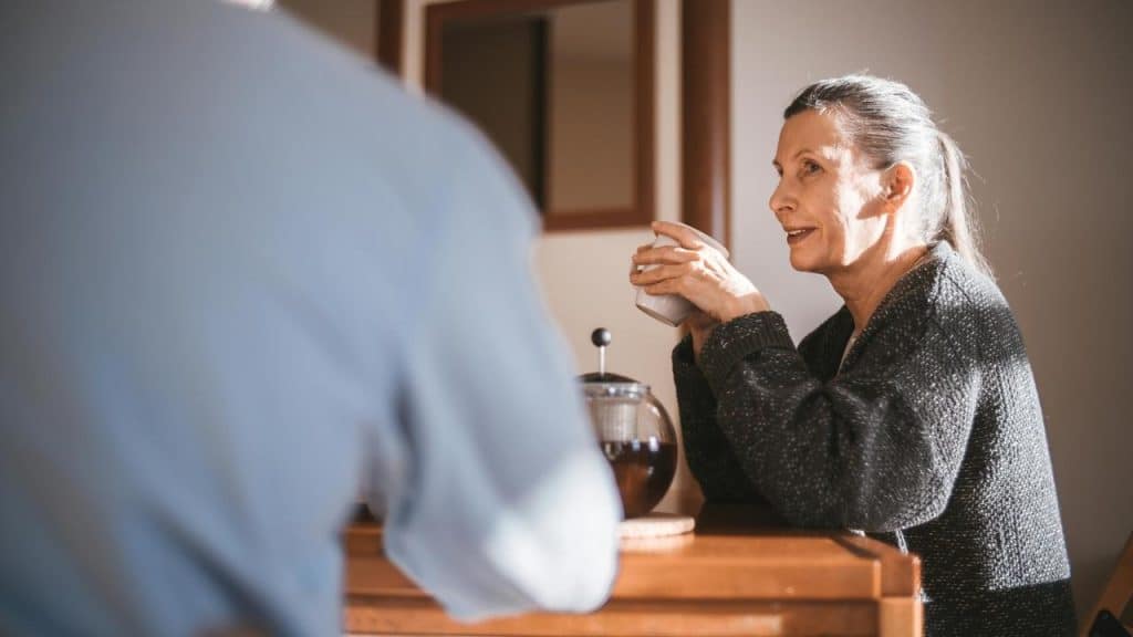 A woman holding a cup and talking to someone at a table.