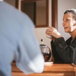 A woman holding a cup and talking to someone at a table.