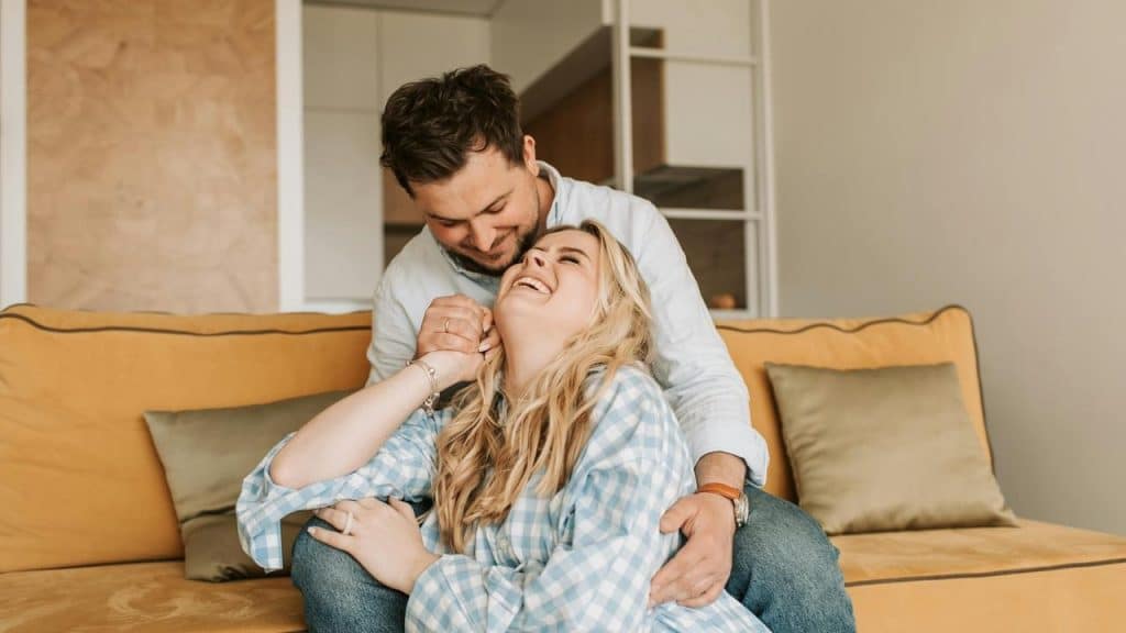 A couple sitting on a couch laughing together.